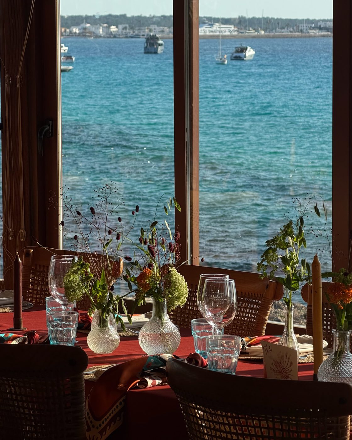 A table laid with scarves in front of a window onto the sea