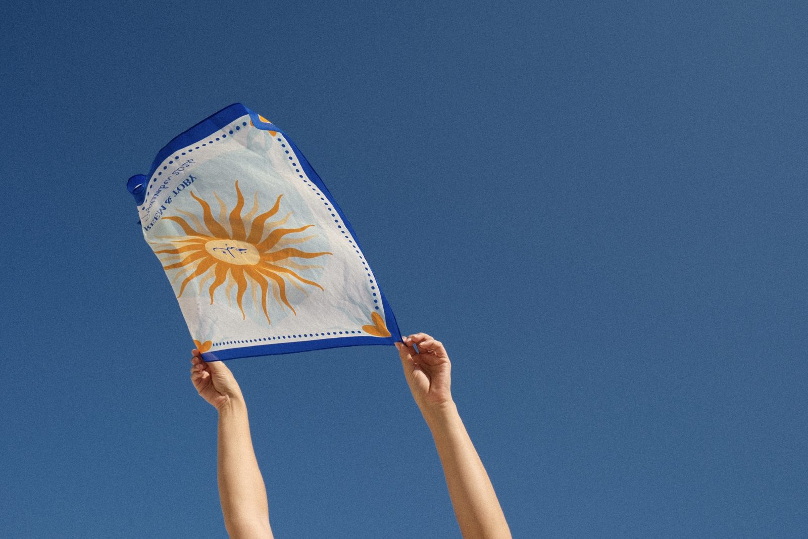 Hands holding the sun scarf up against a blue sky