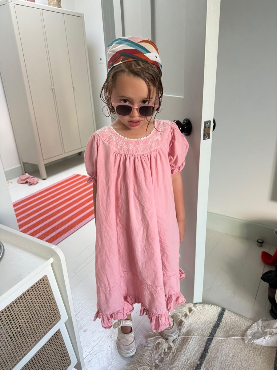A little girl in a pink dress and sunglasses wearing the scarf on her head