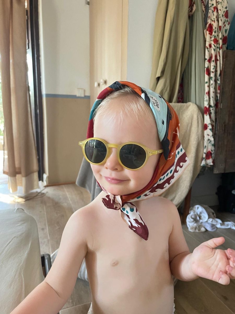 A little one in sunglasses with the scarf tied as a headscarf